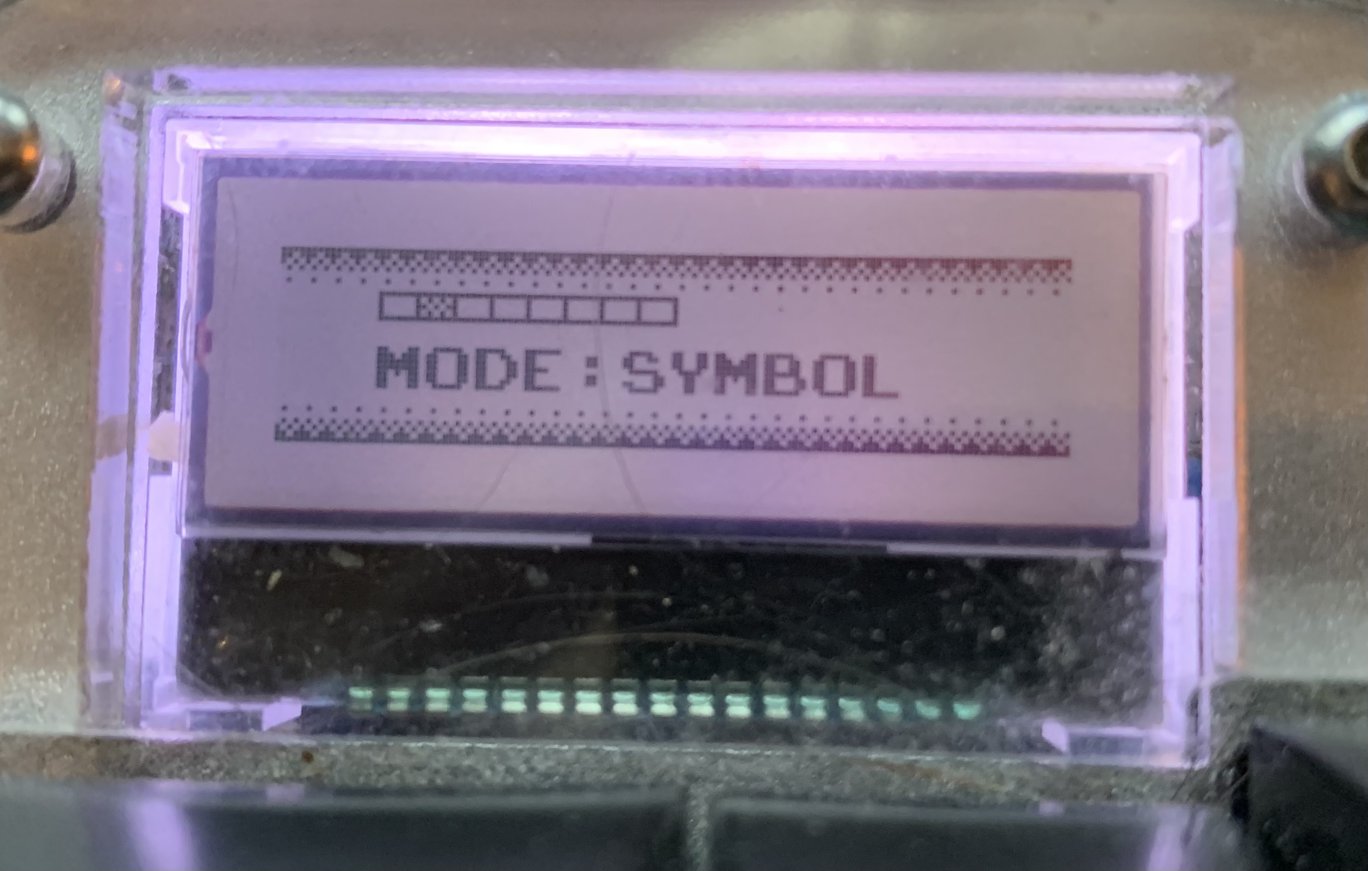 A photo of an LCD display showing the words "Mode: Symbol" with some pixel art styling.